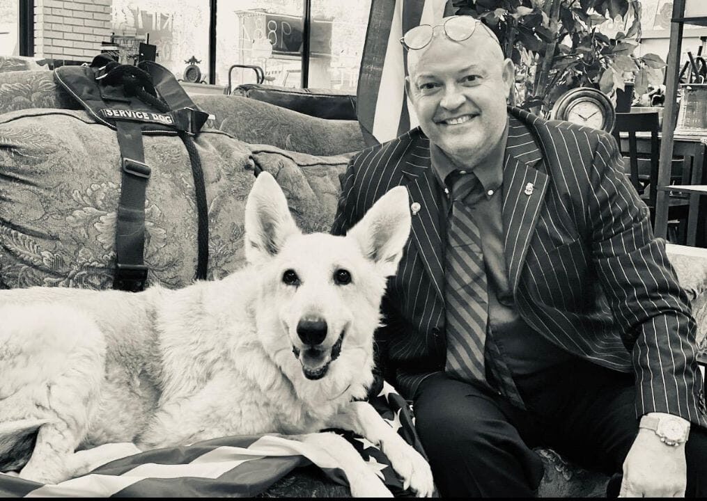 Dr Romano sitting on sofa with white search and rescue service dogs, Laika